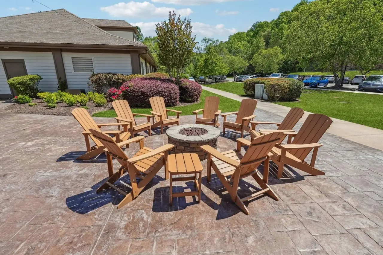 Outdoor firepit lounge at the Achasta clubhouse — eight cedar Adirondack chairs arranged around a stone gas firepit on a stamped concrete patio